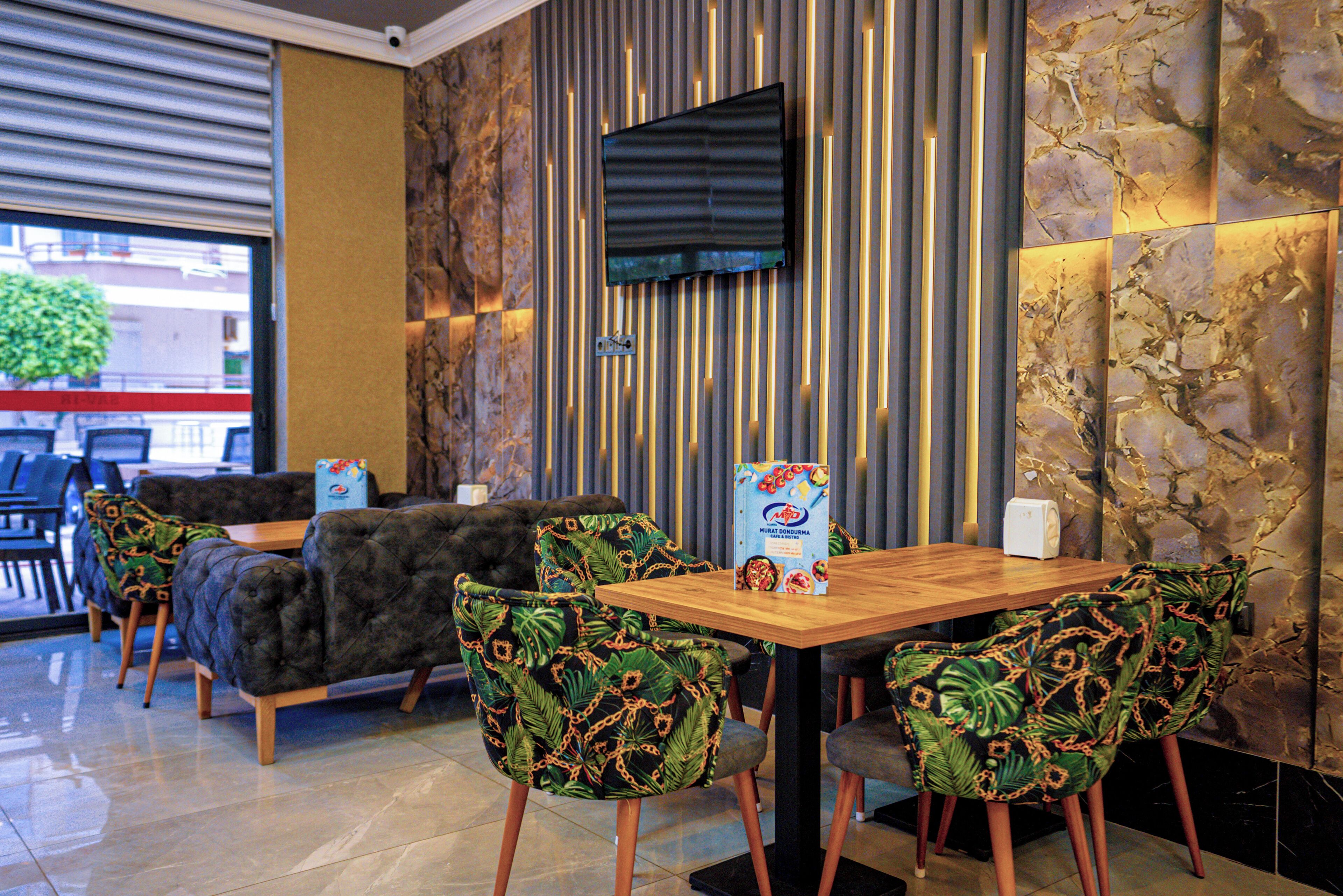 A restaurant with a wooden table and chairs, a sofa, and a TV mounted on the wall.