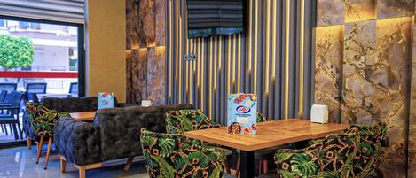 A restaurant with a wooden table and chairs, a sofa, and a TV mounted on the wall.
