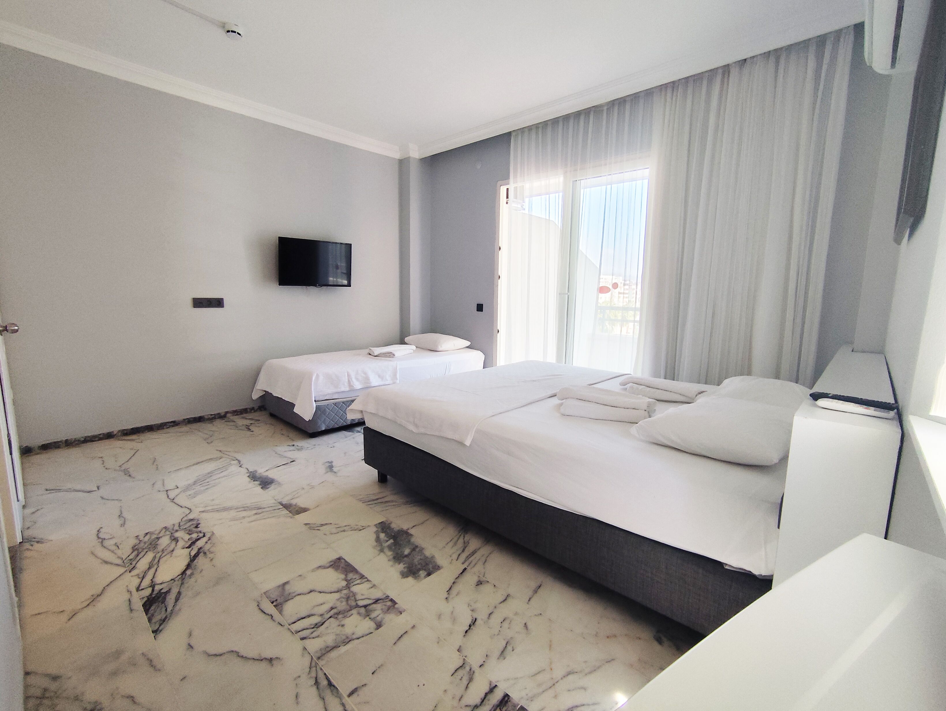 Quarto de hotel com duas camas, televisão de tela plana, uma janela grande com cortinas e piso de mármore.