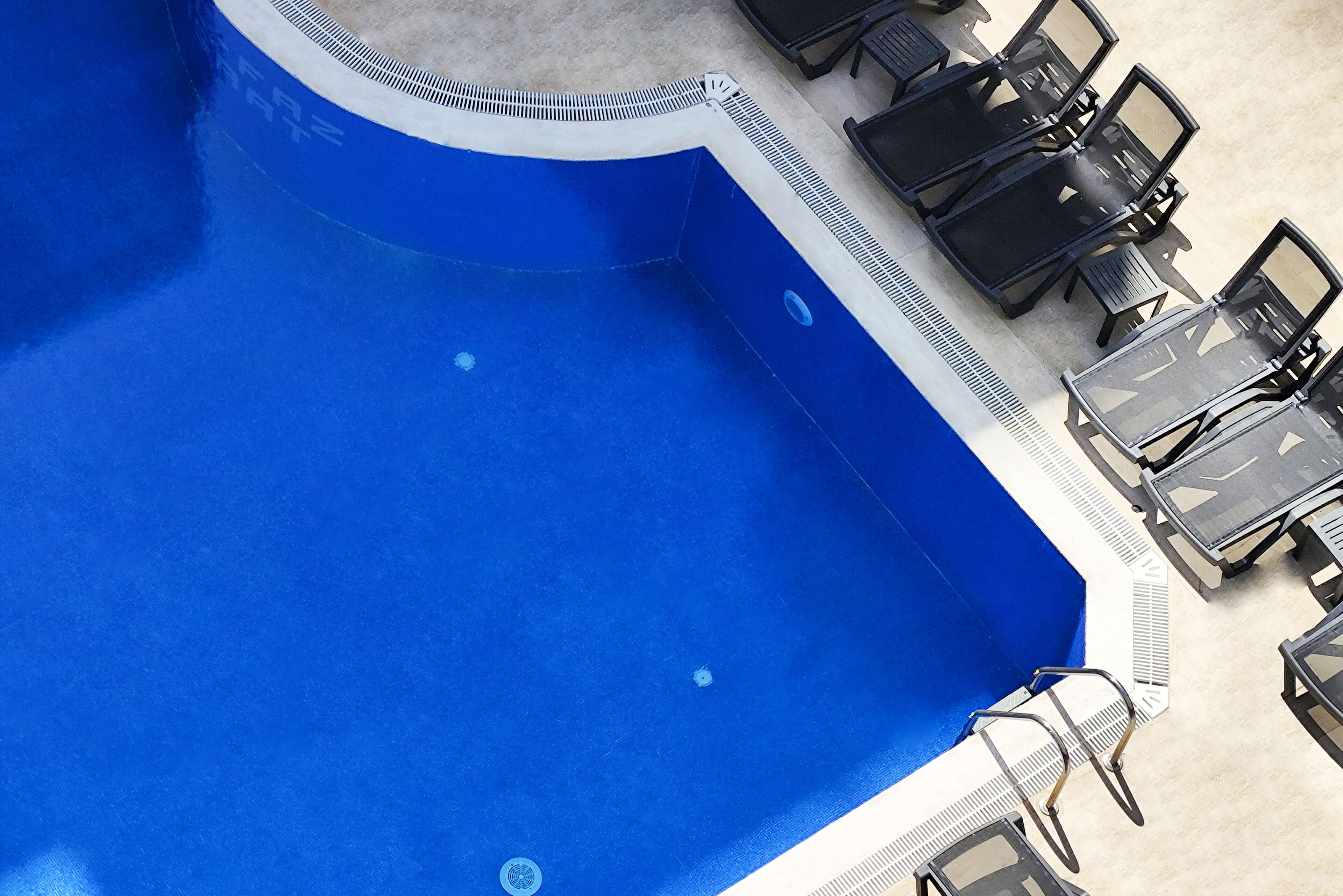 A swimming pool with a blue interior, surrounded by black lounge chairs and tables.