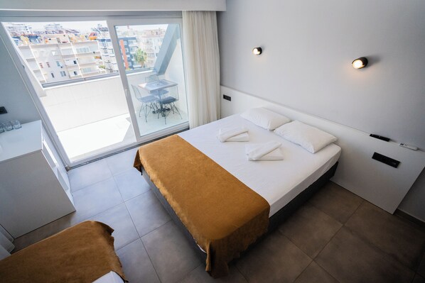 A hotel room with a bed, a small table, and a view of the city through a large window. - Savir Suite Hotel (Alanya)