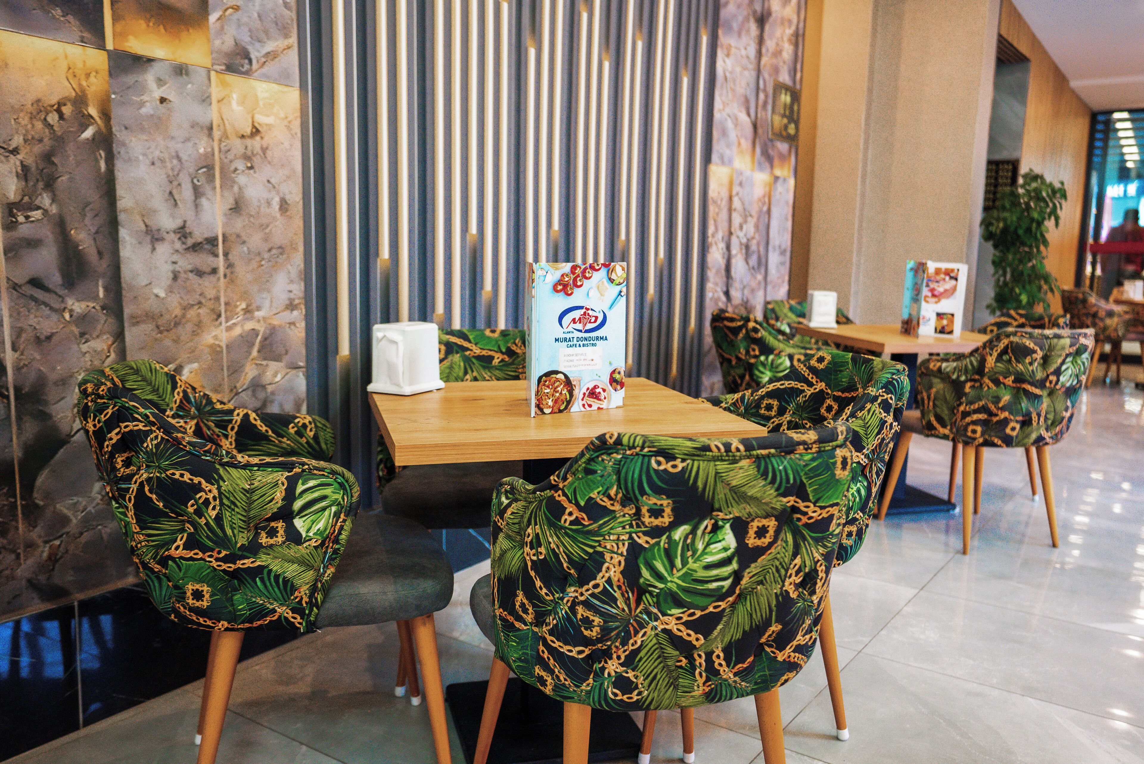 L’intérieur d’un restaurant, avec des chaises à motifs tropicaux, un mur en marbre et un présentoir à menus.