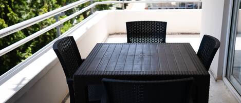 A balcony with a wooden table and two chairs, overlooking a building and greenery.