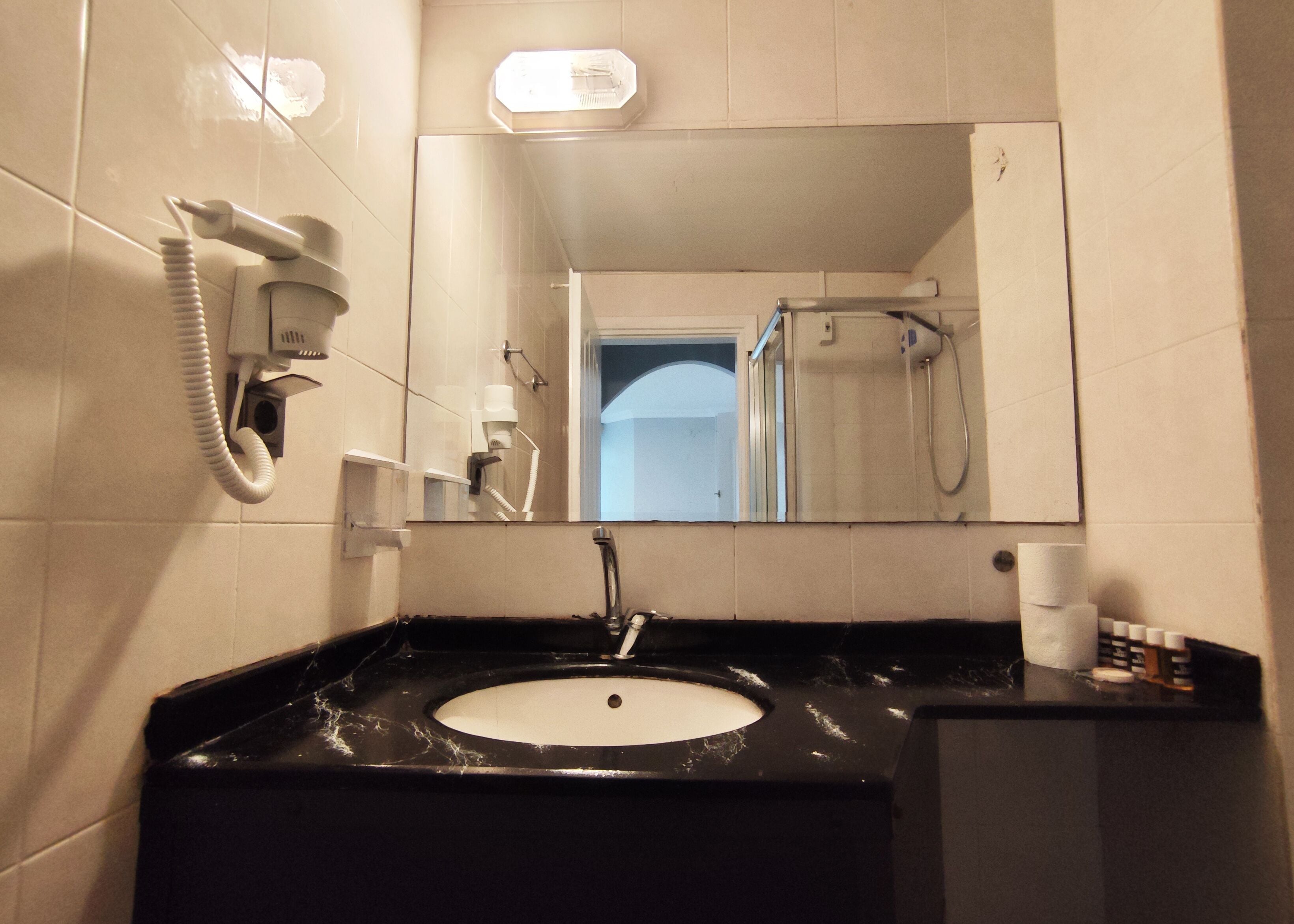 A bathroom with a black sink, a mirror, a hairdryer, and a shower.