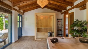 Um espaço de spa com teto de madeira, uma banheira de hidromassagem, uma sauna de madeira e vista para o exterior.
