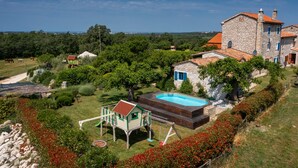 Um edifício de pedra com piscina, cercado por vegetação exuberante e um parquinho.