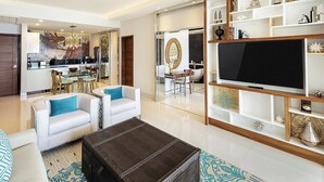 A modern living room with a large flat-screen TV, a coffee table, and a sofa with blue cushions. There is a dining area with a glass table and chairs, and a kitchen in the background. - Dream Cabo Residence with Ocean Views (Cabo San Lucas)