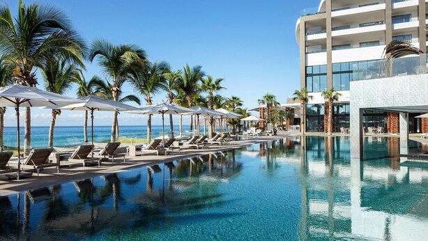 A poolside area with lounge chairs and umbrellas, a clear blue pool, and a view of the ocean. - Dream Cabo Residence with Ocean Views (Cabo San Lucas)