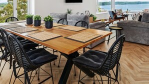 Una sala de estar moderna con una mesa de comedor de madera, sillas negras, sofás grises y un televisor montado en la pared.