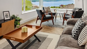 Un salón moderno con vistas al mar, una mesa de centro de madera y asientos cómodos.