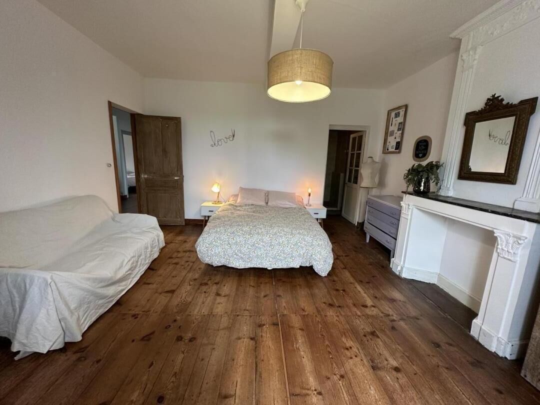 Una camera da letto con pavimento in legno, un letto, una cassettiera, uno specchio e un camino.