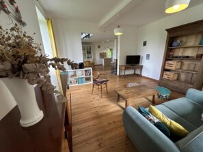 A spacious living room with a wooden floor, a blue sofa, a wooden coffee table, and a television.