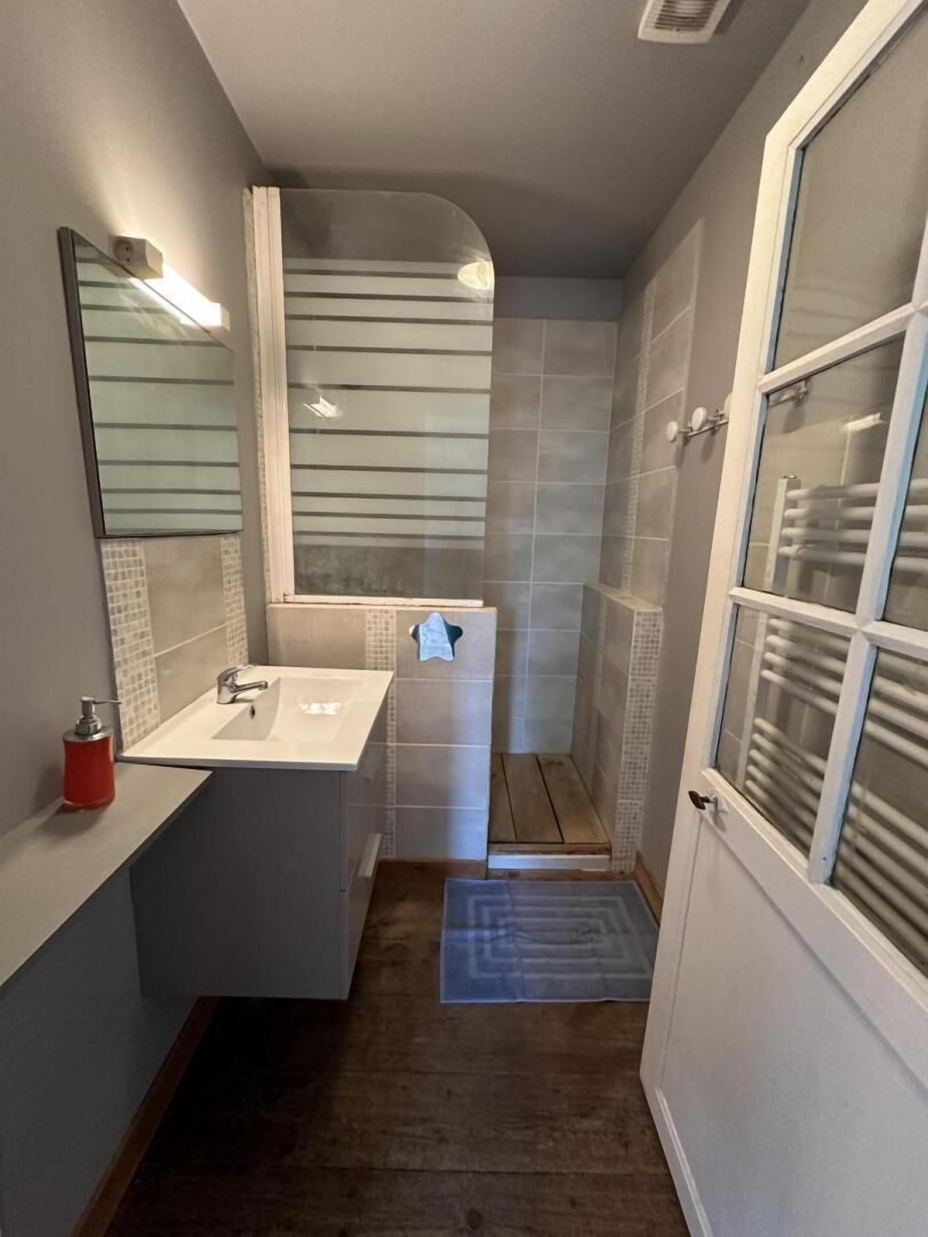 A compact bathroom with a white sink, mirror, and shower area.