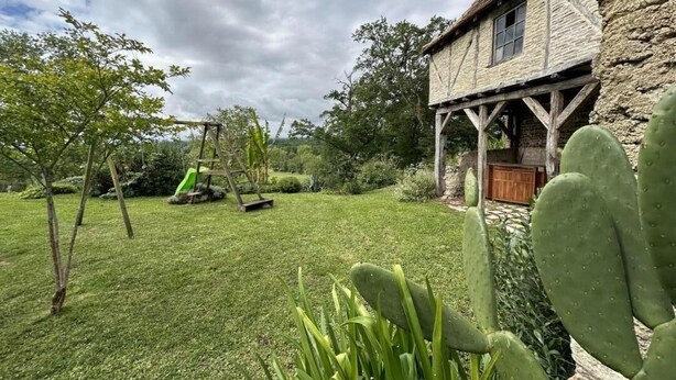 Une maison de campagne en pierre, dotée d’un porche en bois, d’une pelouse bien entretenue et d’un cactus au premier plan.