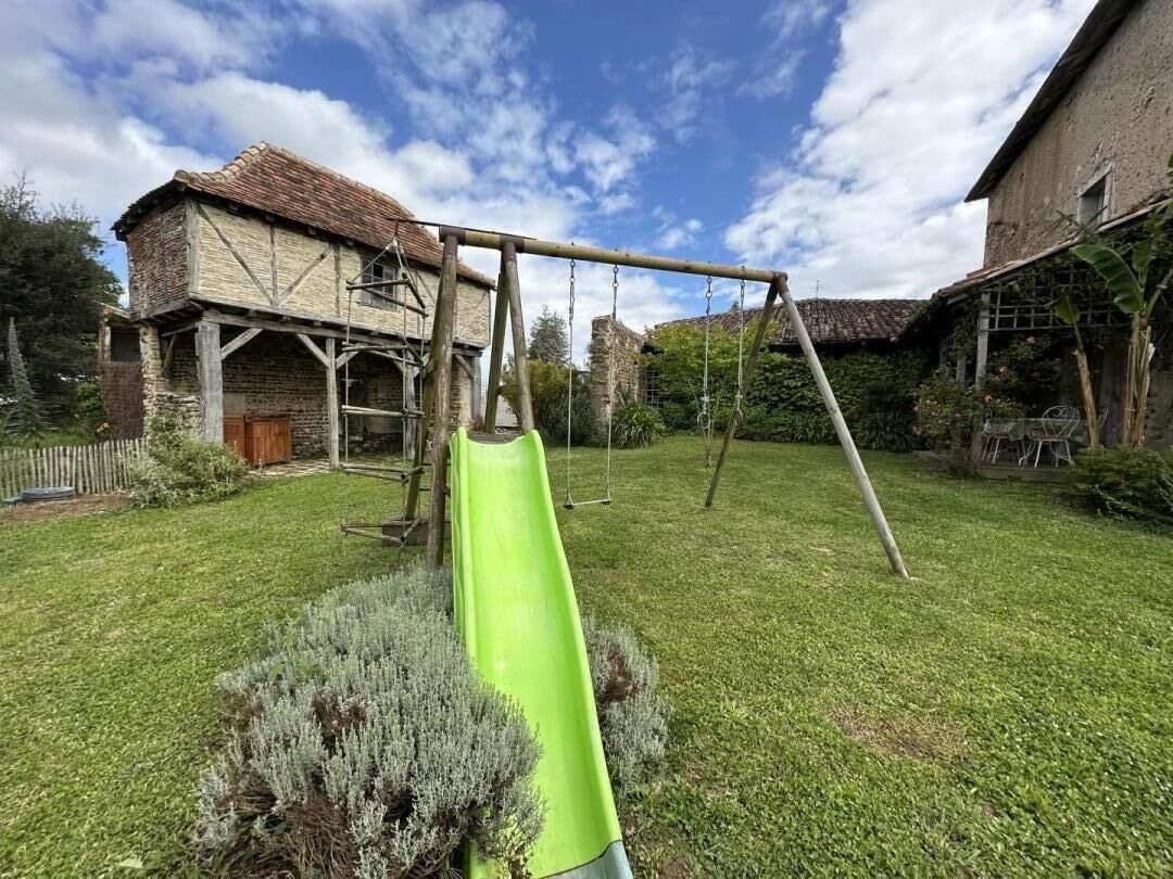 Een speelplaats met een groene glijbaan en schommels in een achtertuin, met een huis op de achtergrond.