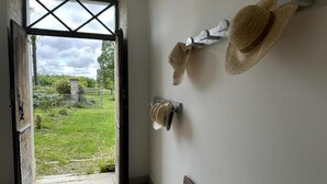 Une porte ouverte donnant sur un jardin, avec un banc et des chapeaux accrochés au mur.