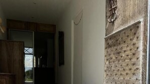 Un couloir avec une porte en bois rustique, un sol en pierre et une vue sur un jardin fleuri.