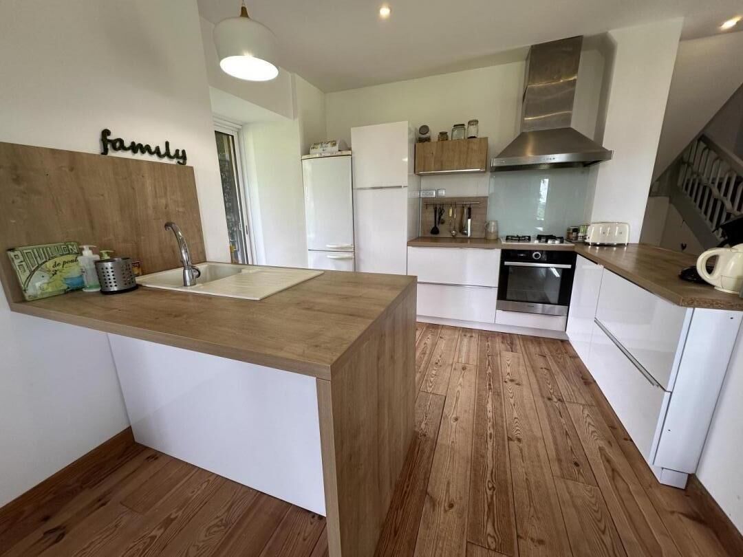 Una cocina moderna con armarios blancos, encimera de madera, campana extractora de acero inoxidable y horno integrado.