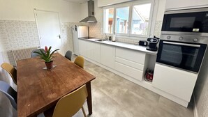 A modern kitchen with white cabinets, a wooden dining table, and a built-in oven. - Le Gîte du Sequé - Saint Pandelon (SAINT PANDELON)