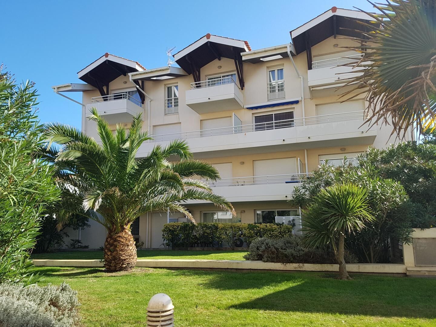 A multi-story building with balconies, surrounded by well-maintained greenery and palm trees.