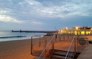 A beach with a pier extending into the water, a staircase leading to a building with yellow lighting, and a sandy shoreline. - La Croisière - Capbreton (CAPBRETON)