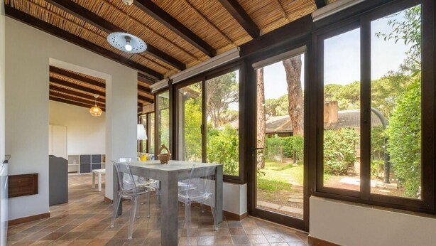 A spacious dining area with a large table and chairs, a ceiling with wooden beams, and large windows offering a view of a garden. - Fiorenza's charming beach house (Pula)