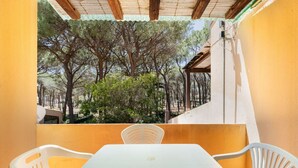 Un balcone con tavolo e sedie, affaccia su un giardino con alberi e un edificio sullo sfondo.