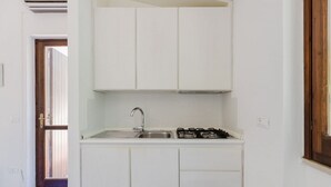 Una cucina compatta con pensili bianchi, un lavello in acciaio inossidabile e un piano cottura a gas.