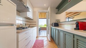 Cucina piccola con mobili bianchi, un elettrodomestico rosso e vista su un patio esterno.