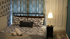 Una cama bien hecha con ropa de cama estampada, una lámpara de noche y una ventana con cortinas.