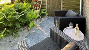 An outdoor patio with wicker furniture, a small table with a glass and bottle, and a wooden fence with potted plants. - Cozy home in Noordscheschut with WiFi (Noordscheschut)