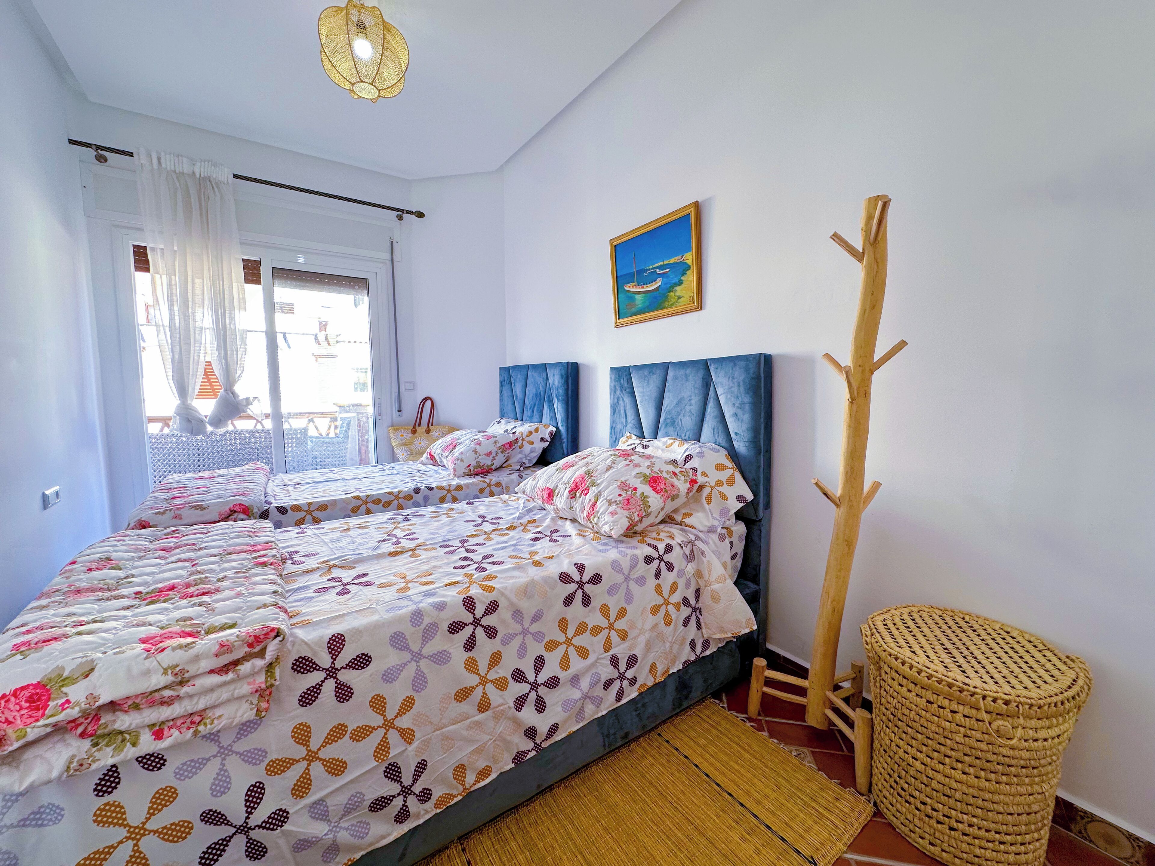 Une chambre à coucher avec un lit, une fenêtre avec des rideaux, un tableau et une chaise en bois.