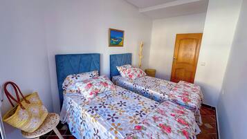 Un dormitorio con dos camas, una puerta de madera, una mesita pequeña y una silla.