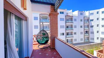 Un balcón con una silla colgante, suelo de baldosas y vistas a edificios vecinos.