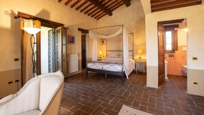 Una camera da letto con un letto a baldacchino, una zona relax con una poltrona e un bagno con il water e un lavandino.