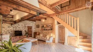 Un interior rústico con pared de piedra, vigas de madera, un sofá, un televisor y una escalera.