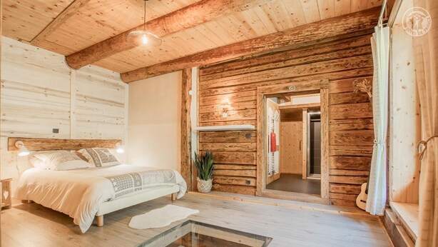 Una habitación acogedora de madera con una cama, una mesa de centro de vidrio y una puerta que da a otra habitación.