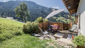Una terraza de madera con mesa y sillas, con vistas a un paisaje montañoso.