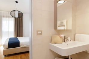 A hotel room with a bed, a white sink, a mirror, and a hanging light fixture. - Alba sul mare - Portopiccolo Apartments (Duino-Aurisina)