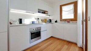A modern kitchen with white cabinetry, a built-in oven, and a window with a wooden frame.