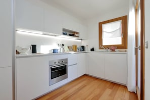 Una cocina moderna con armarios blancos, horno empotrado y ventana con marco de madera.