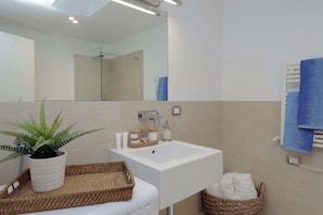 Un baño con lavamanos blanco, un espejo, una planta en maceta, un perchero y una cesta.