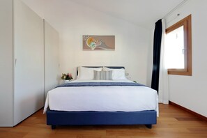 Un dormitorio con cama, un cuadro, una ventana y una puerta.