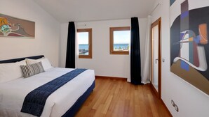 A hotel room with a bed, two windows, a door, and a painting on the wall.