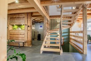 Interior de madera con una escalera de caracol, una pared de troncos y una pared verde con una planta.