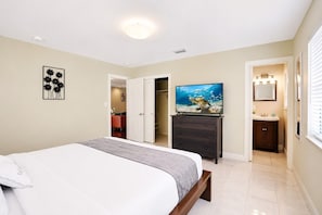 Un dormitorio con cama, cómoda, televisor y baño visible a través de una puerta abierta.