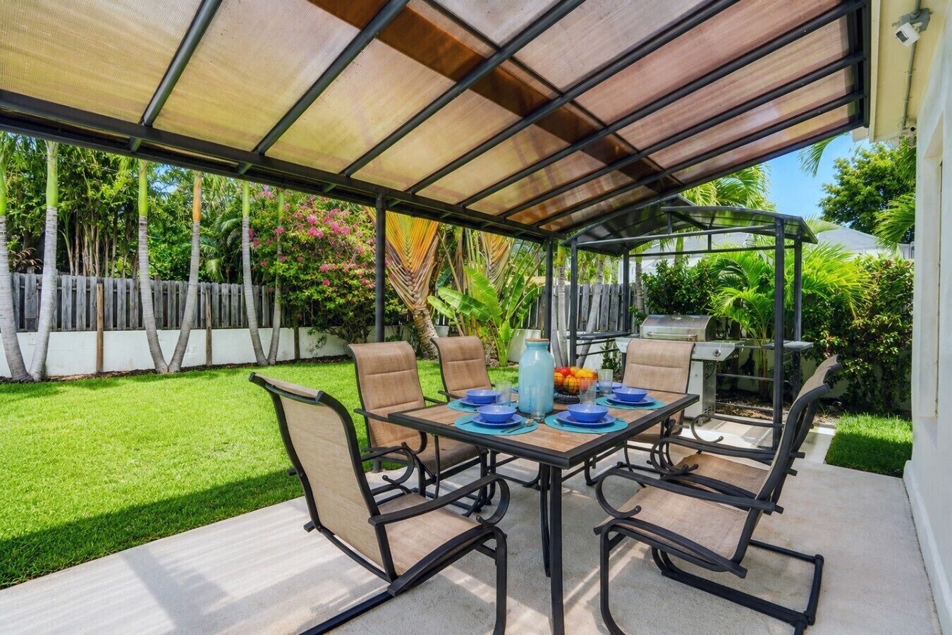 A covered patio with a table and chairs, surrounded by a well-maintained lawn and a wooden fence.