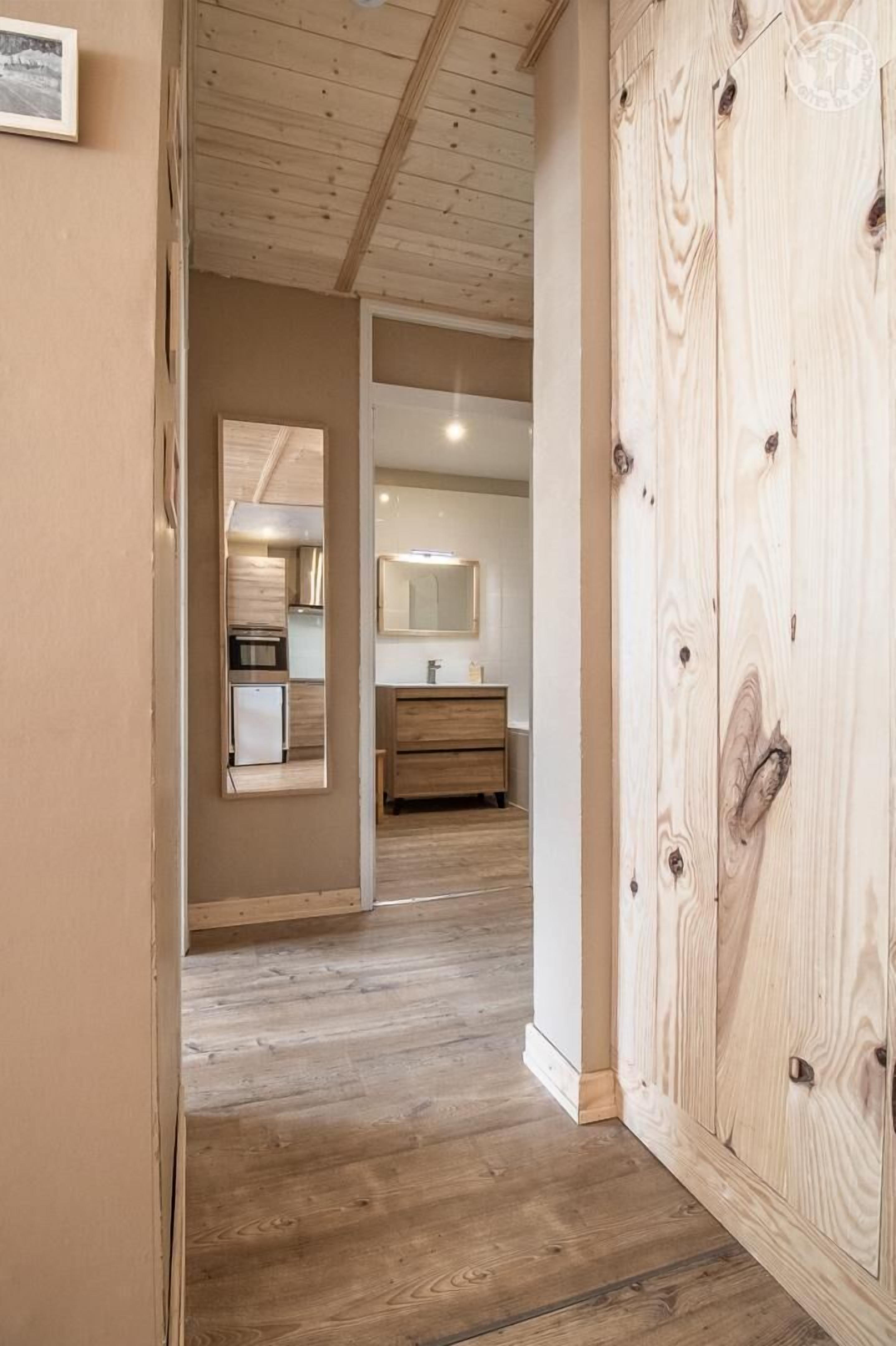 Un couloir doté d’un plancher en bois, d’une armoire en bois et donnant sur un coin cuisine avec un réfrigérateur et un évier.