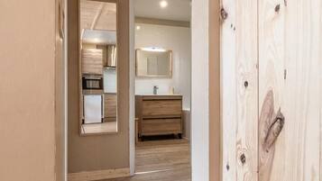 Un couloir doté d’un plancher en bois, d’une armoire en bois et donnant sur un coin cuisine avec un réfrigérateur et un évier.