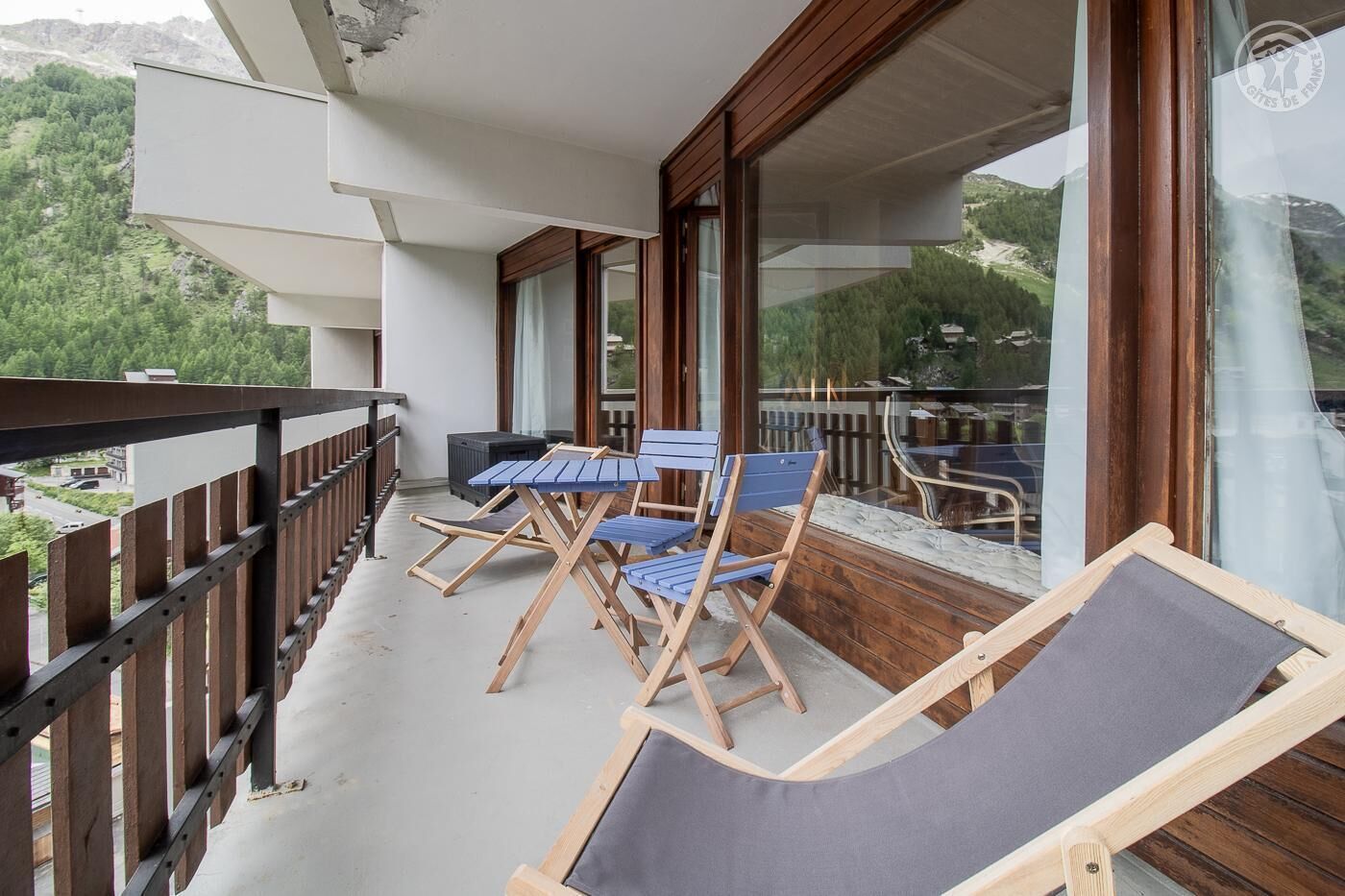 Ein Balkon mit Holzkufen und Tisch, mit Blick auf eine gebirgige Landschaft.